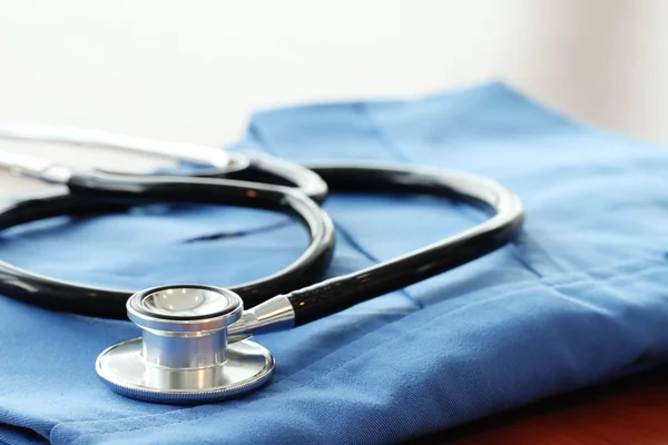 Stethoscope with blue doctor coat on wooden table with shallow D — Stock Photo, Image