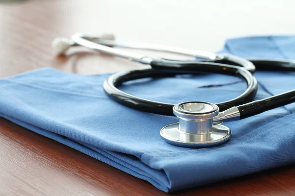 Stethoscope with blue doctor coat on wooden table with shallow D — Stock Photo, Image