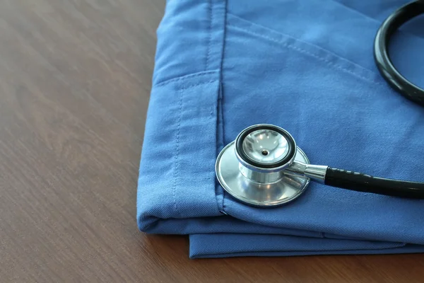 Estetoscopio con abrigo médico azul sobre mesa de madera con D poco profunda — Foto de Stock