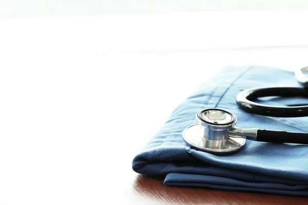 Estetoscopio con abrigo médico azul sobre mesa de madera con D poco profunda — Foto de Stock