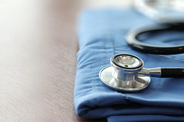 Estetoscopio con abrigo médico azul sobre mesa de madera con D poco profunda — Foto de Stock