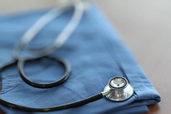 Estetoscopio con abrigo médico azul sobre mesa de madera con D poco profunda — Foto de Stock