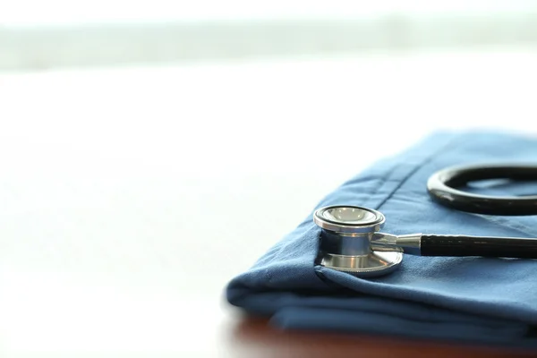 Estetoscopio con abrigo médico azul sobre mesa de madera con D poco profunda — Foto de Stock