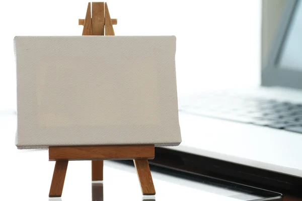 Blank canvas and wooden easel on laptop computer as concept — Stock Photo, Image