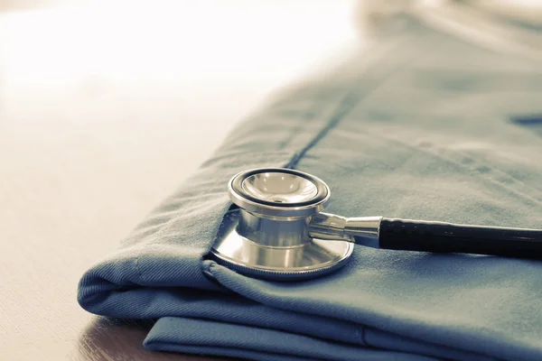 Estetoscopio con abrigo médico azul sobre mesa de madera con D poco profunda — Foto de Stock