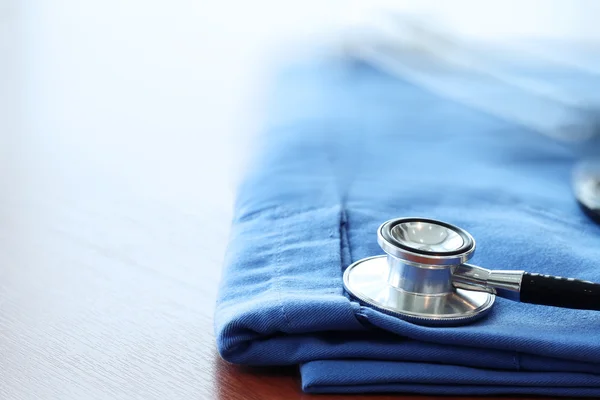 Estetoscopio con abrigo médico azul sobre mesa de madera con D poco profunda — Foto de Stock