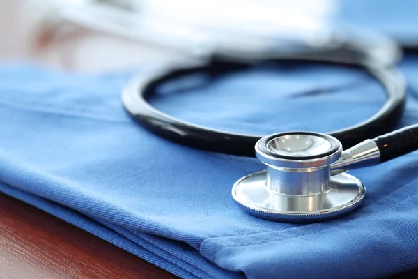 Estetoscopio con abrigo médico azul sobre mesa de madera con D poco profunda — Foto de Stock