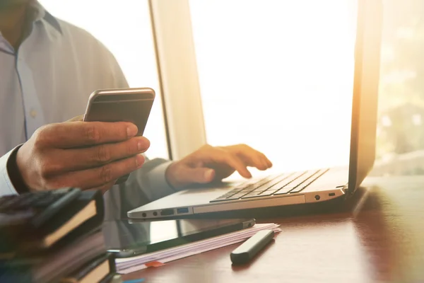 Main d'homme d'affaires en utilisant un ordinateur portable et un téléphone mobile sur un bureau en bois comme — Photo