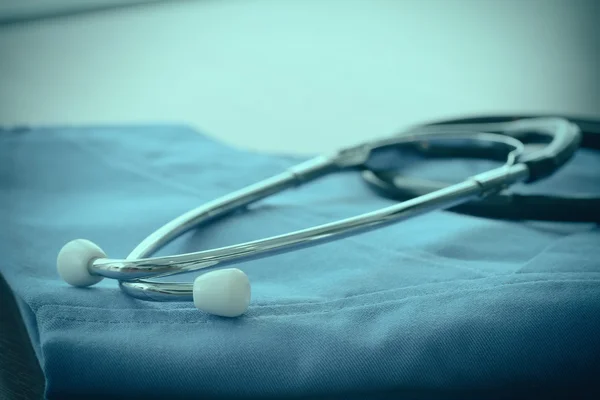 Estetoscopio con abrigo médico azul sobre mesa de madera con D poco profunda — Foto de Stock