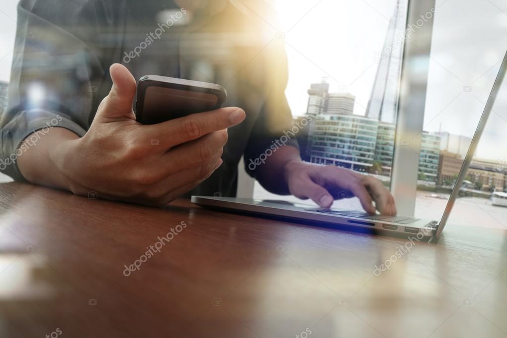 designer hand working and smart phone and laptop on wooden desk 