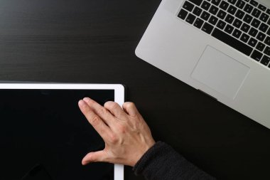  Koyu ahşap bir masadaki dizüstü bilgisayarın yanındaki ekrana dokunan dijital tablet kullanan birinin yakın plan fotoğrafı..