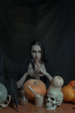 Güzel gotik kız siyah arka planda balkabaklarıyla poz veriyor.