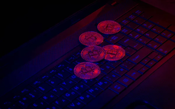 Bitcoins laying on a laptop keyboard in neon lights