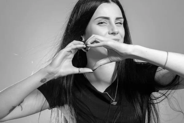 Beautiful young girl making heart sign with hands over grey background