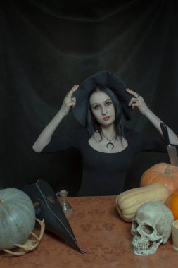 Cadı şapkalı güzel kız karanlık arka planda poz veriyor.