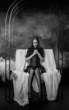 Güzel gotik kız karanlık arka planda bir bankta oturuyor.