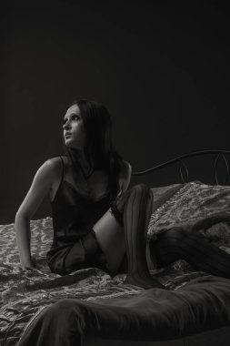 Yatakta oturan siyah elbiseli güzel bir kadın.