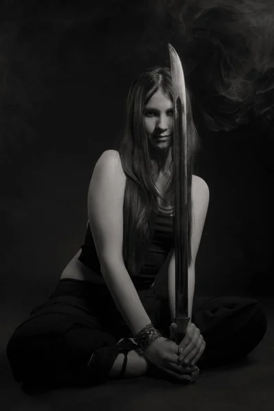美丽的女人 背着剑坐在黑暗的背景上 — 图库照片