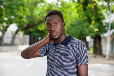 Dışarıda dikilip el ele kameraya bakan Afrikalı genç bir adamın portresi..