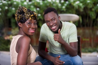 Genç bir çift parkta oturmuş kameraya bakıp gülümsüyor..