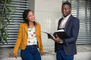 Genç iş adamları dışarıda durmuş, gülümseyen belgelere bakıyor..