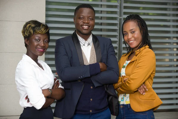 Bir grup genç iş adamı ofiste durmuş kameraya bakıyor ve kollarını kavuşturup gülümsüyor..