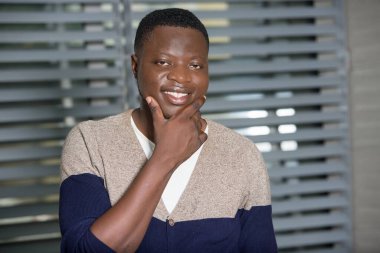 Mutlu genç bir adam, dişlek bir gülümsemeyle yanağına dokunuyor ve sakalını tıraş etmekten memnun.