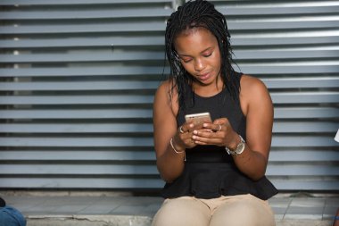 Açık havada akıllı telefonuyla gülümseyen genç bir kadın. Şehir bağlamında siyah elbiseli bir kız ve dışarıda oturan ve cep telefonu kullanan bir iş kadını. Teknoloji konsepti