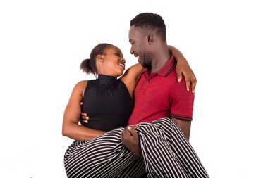 Beyaz arka planda kırmızı tişörtlü genç bir adam kız arkadaşını kollarında tutarak gülüyor..