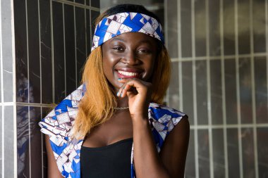 Duvarın yanında duran genç bir kadın kameraya bakıp gülümsüyor..