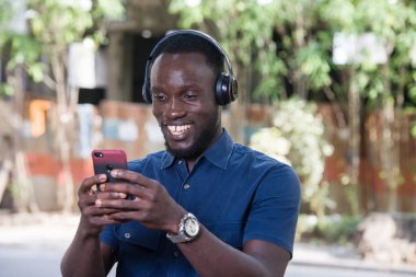 Adam kulaklıkla dışarıda cep telefonu kullanarak müzik dinliyor..