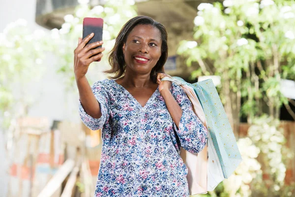 Молодая Женщина Стоящая Улице После Покупок Глядя Мобильный Телефон Улыбаясь — стоковое фото
