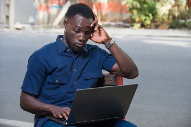 Delikanlı dışarıda dizüstü bilgisayarla oturmuş düşünüyor..