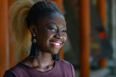 Mor tişörtlü genç kız kameraya bakıp gülümsüyor..