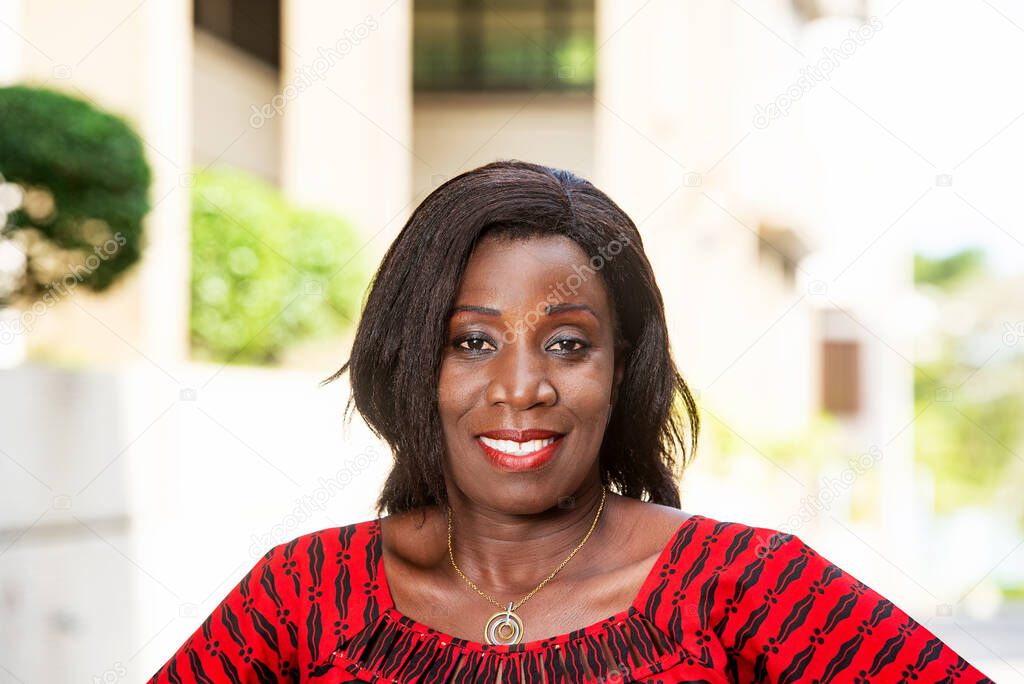 mature african woman standing outdoors looking at camera smiling.