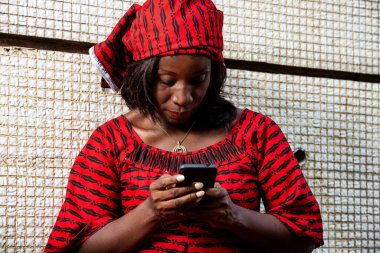 Peştamallı olgun bir kadın duvarın yanında durmuş cep telefonuna bakıyor..