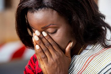Young woman in red outfit, looking thoughtful and frustrated, hands on her face meditating or crying with her eyes closed on the street