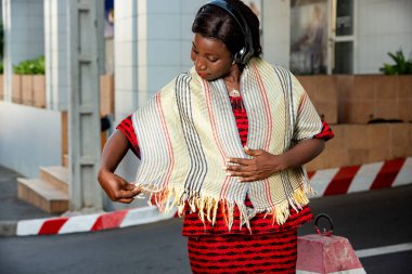 Kırmızı peştamallı güzel, yetişkin bir iş kadını. Kulaklığıyla müzik dinlerken boynuna dolanmış güzel eşarbına hayran.