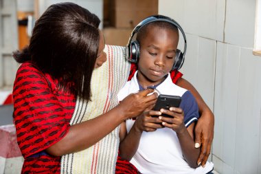 Geleneksel elbiseli olgun bir kadın açık havada oturmuş cep telefonu kullanarak müzik dinleyen çocuğunun düğmesini ayarlıyor..