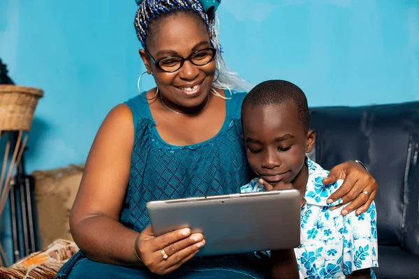 Africká Hospodyňka Dívá Něco Digitálním Tabletu Svým Chlapcem Sedí Křesle — Stock fotografie