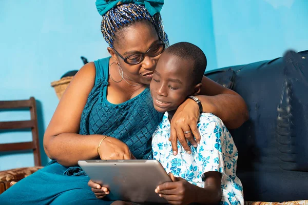 Africká Hospodyňka Ukazuje Něco Digitálním Tabletu Svému Chlapečkovi Sedícímu Křesle — Stock fotografie