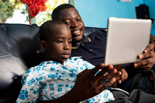 Mladý Afričan Sedí Křesle Obývacím Pokoji Dítětem Spolu Sledují Digitální — Stock fotografie