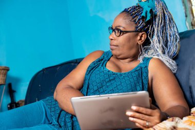 Gözlüklü olgun bir kadın elinde kanepede uzanmış gülümseyen bir şey izliyor..