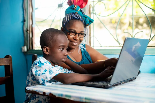 Mutlu Afrikalı anne, oğluyla aynı masada oturmuş bilgisayarla gülümsüyor.