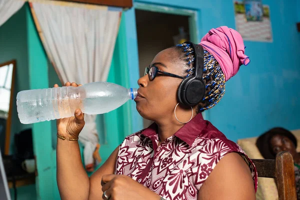 美しいアフリカの女性は喉が渇き ペットボトルにミネラルウォーターを飲み ヘッドフォンで音楽を聴き — ストック写真