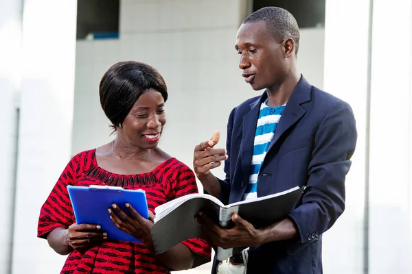 handsome african businessman and beautiful african woman, working outdoors with documents and folders, outdoors on the street while smiling