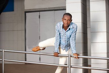 Geleneksel kıyafetli genç adam demir çubuktan atlıyor ve gülümseyen kameraya bakıyor..