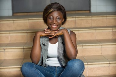 Zarif ceketli ve merdivenlerde oturan gülümseyen genç kadın..