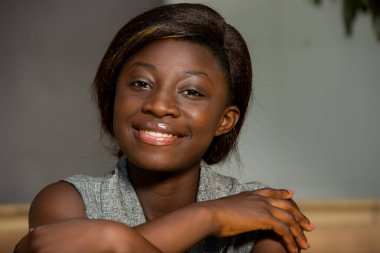 Gri gecelikte oturan genç kız kameraya bakıp gülümsüyor..