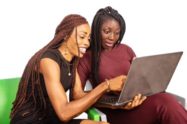 İki güzel genç bayan beyaz arka planda oturuyor ve gülümserken dizüstü bilgisayarla çalışıyorlar..